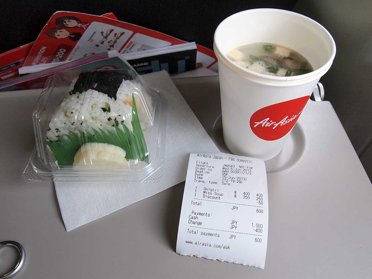 Un repas d'onigiri et de soupe miso est présenté sur une tablette d'avion, avec un reçu imprimé pour le repas à côté.