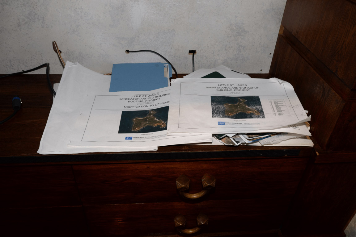 Un bureau en bois est couvert de piles de plans et de documents, dont certains détaillent un projet de construction.